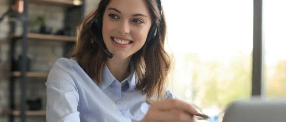 Foto de una mujer sonriente atendiendo el teléfono y con un ordenador