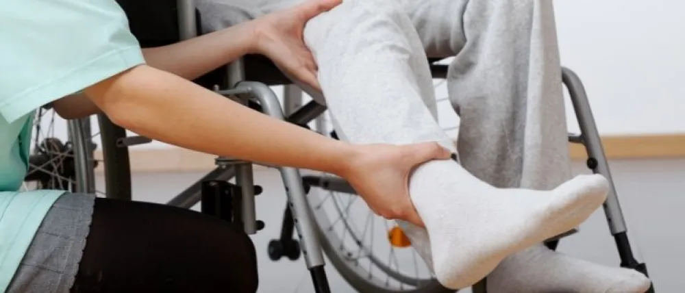 Foto de un fisioterapeuta ayudando a hacer ejercicios con la pierna de una persona en silla de ruedas