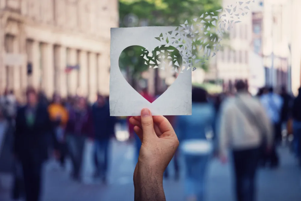 Foto de personas en la calle y una mano que sostiene un hoja con un corazon transparente