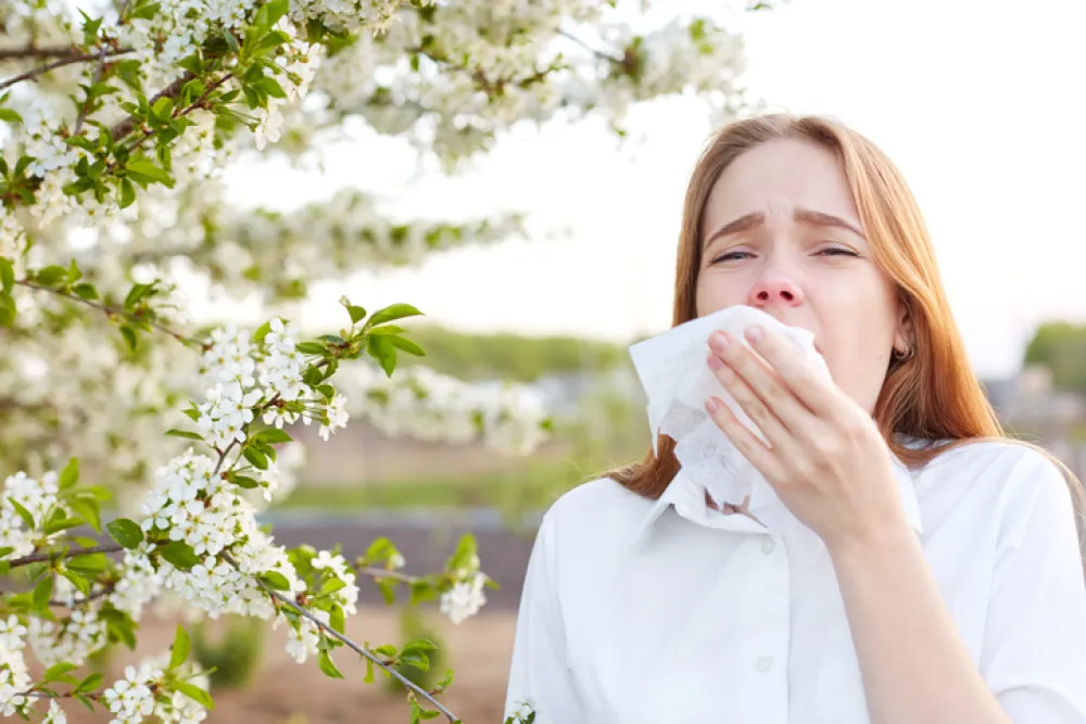 Foto de una mujer en un parque y con un pañuelo mientras estornuda