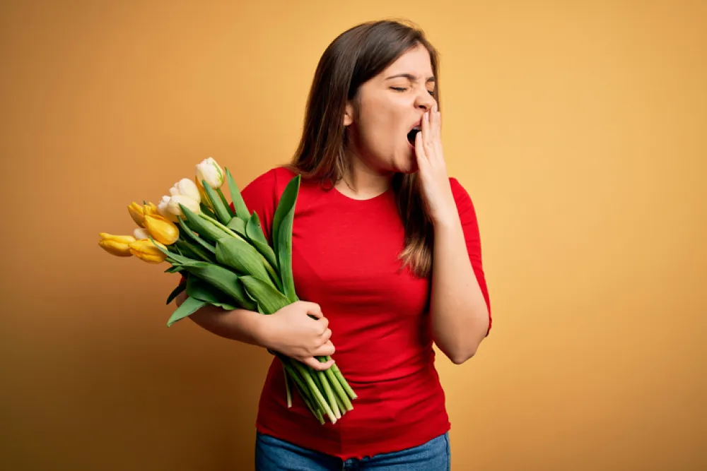 Foto de una mujer que sostiene unas flores mientras bosteza por cansancio
