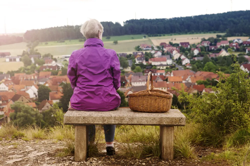 Foto de una señora mayor sentada en un banco mirando el campo
