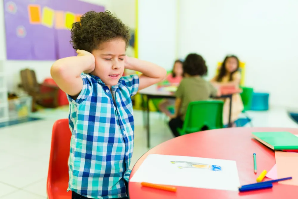 Foto de una clase con un niño pequeño que se tapa los oídos y cierra los ojos