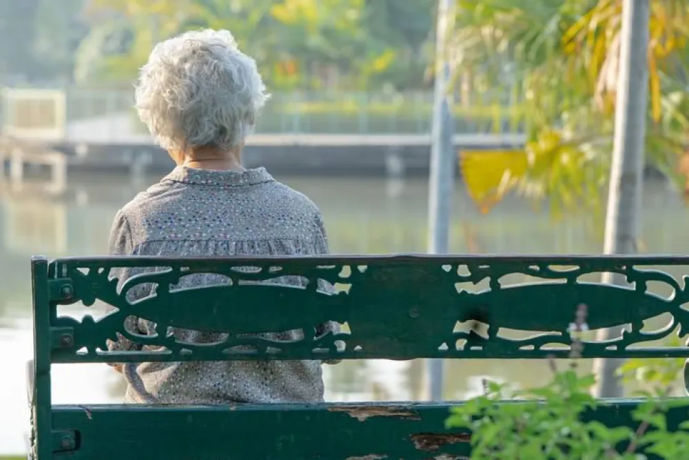 Mujer mayor sentada en un banco mirando a un lago