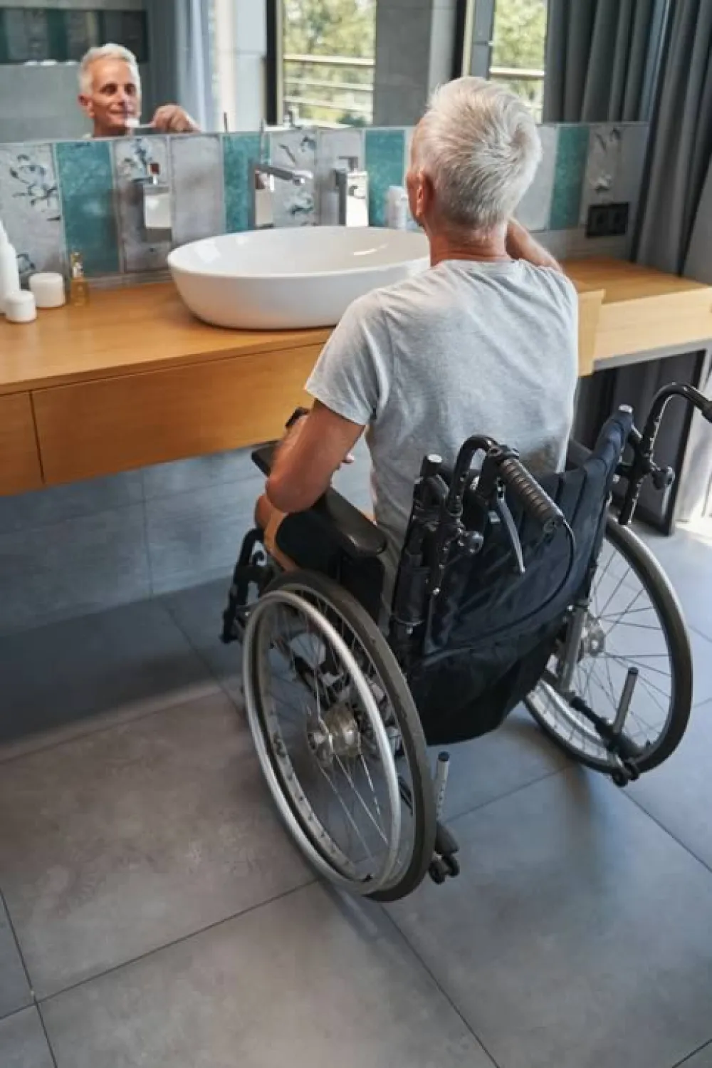 Un hombre en silla de ruedas se lava los dientes mirándose al espejo del baño