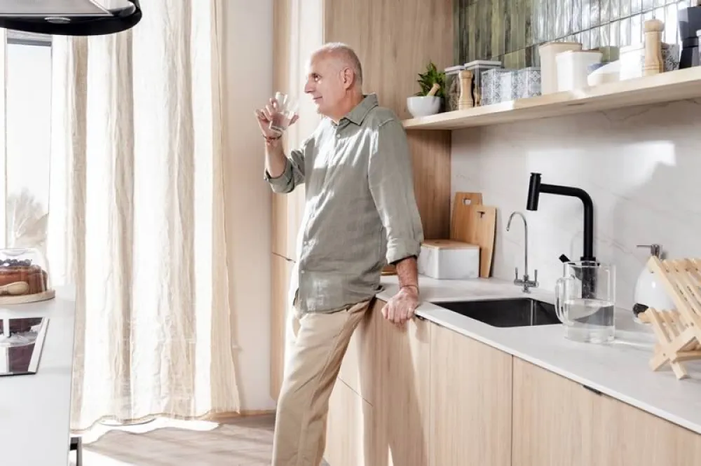 Hombre mayor bebiendo un vaso de agua en una cocina moderna bien equipada